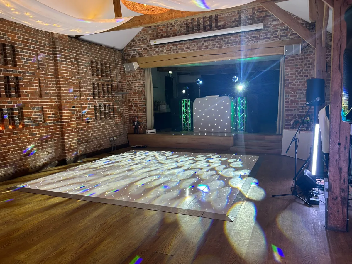 Wedding guests beside a white DJ booth in a barn venue